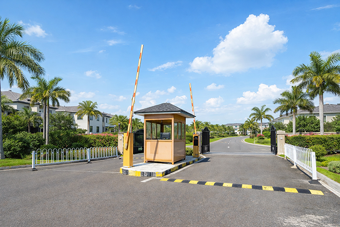 Traditional HOA guard booth at Florida gated community entrance with barrier arms raised